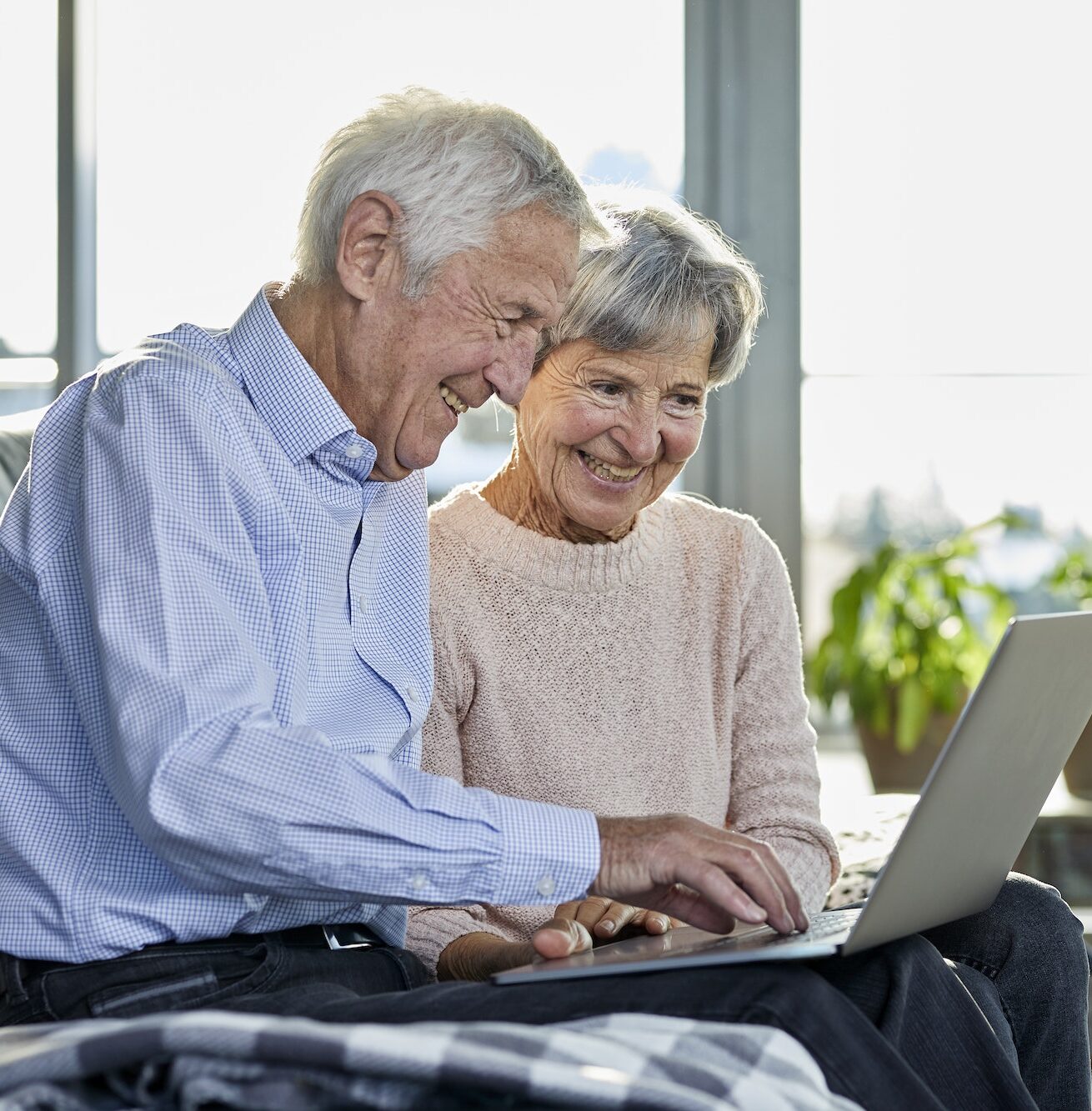 Senior couple sitting together on couch using laptop